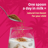 Spoonful of brown powder being sprinkled into milk for a child's natural iron boost.